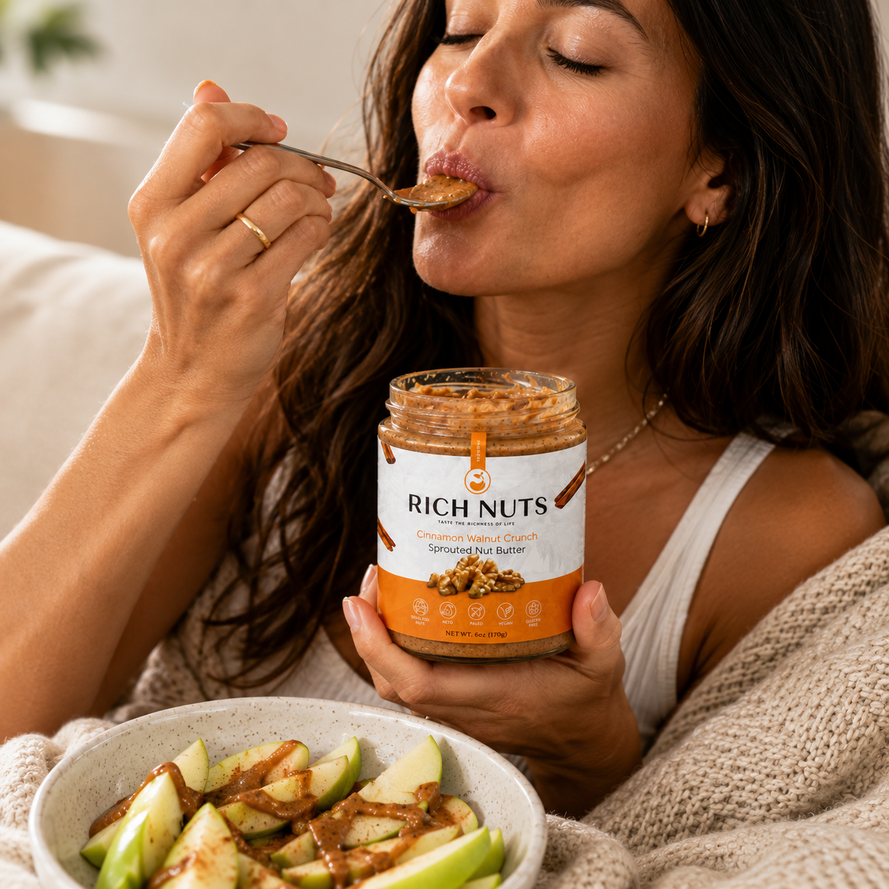 Woman eating Cinnamon Walnut Crunch Sprouted Nut Butter off a spoon with apple slices and nut butter drizzle